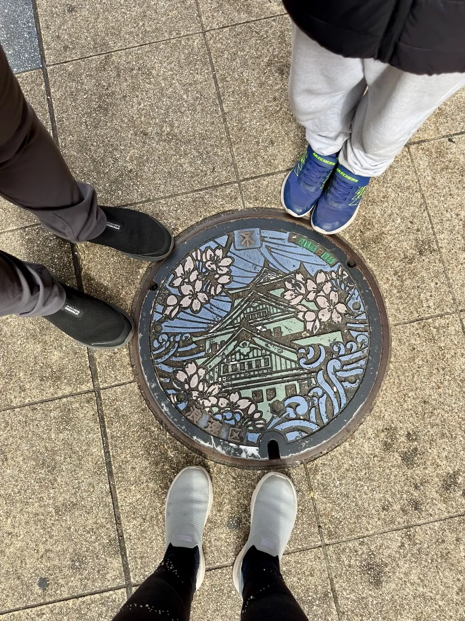 Decorative manhole cover with Osaka Castle and cherry blossoms on a sidewalk